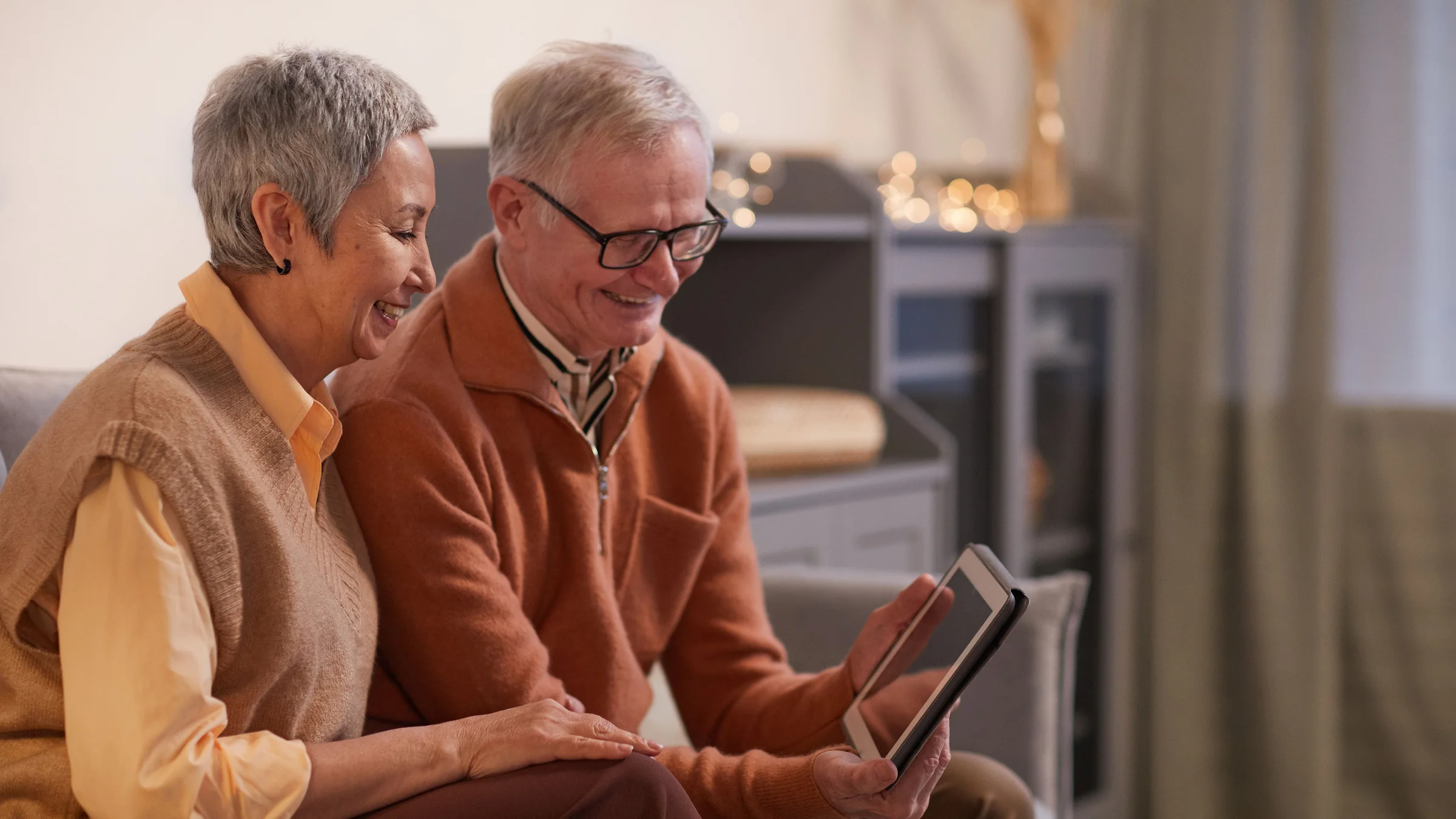 An older couple on the sofa, smiling at a tablet together