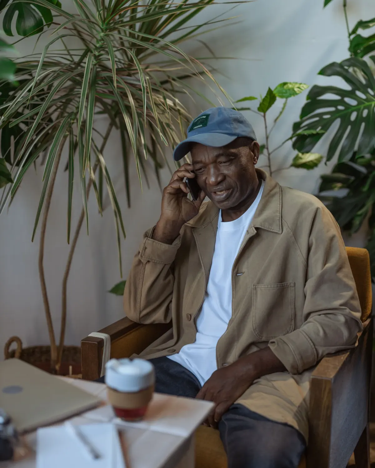 An older man in a cap smiling as he talks on the phone in his armchair