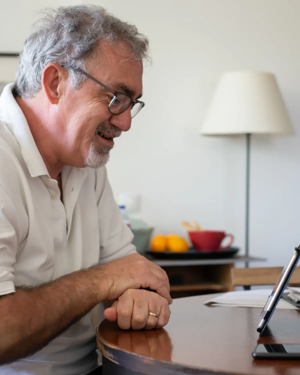 An older man smiling at a video call on a tablet at his dining table