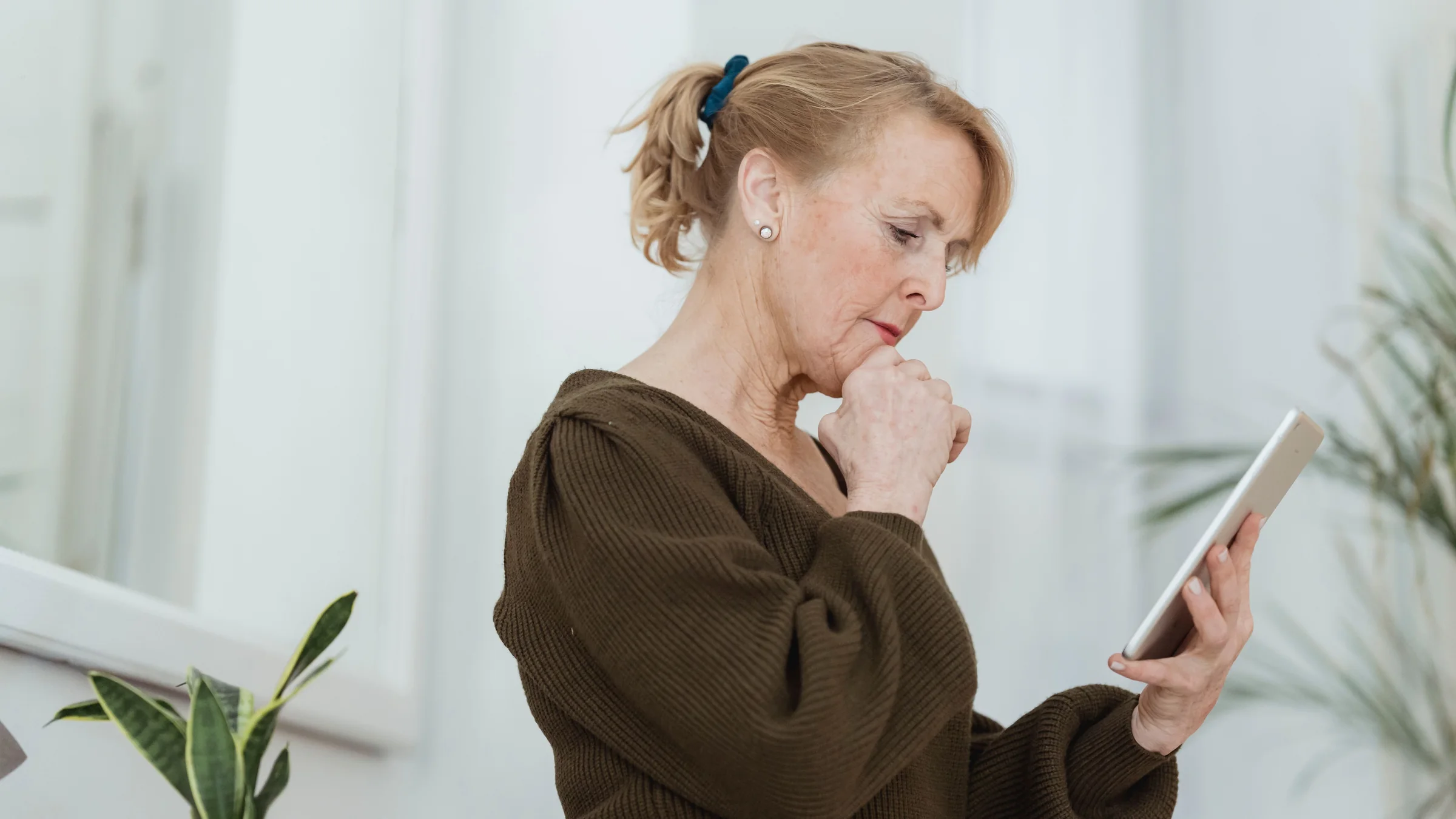An older woman looking carefully at her tablet, with her hand at her chin