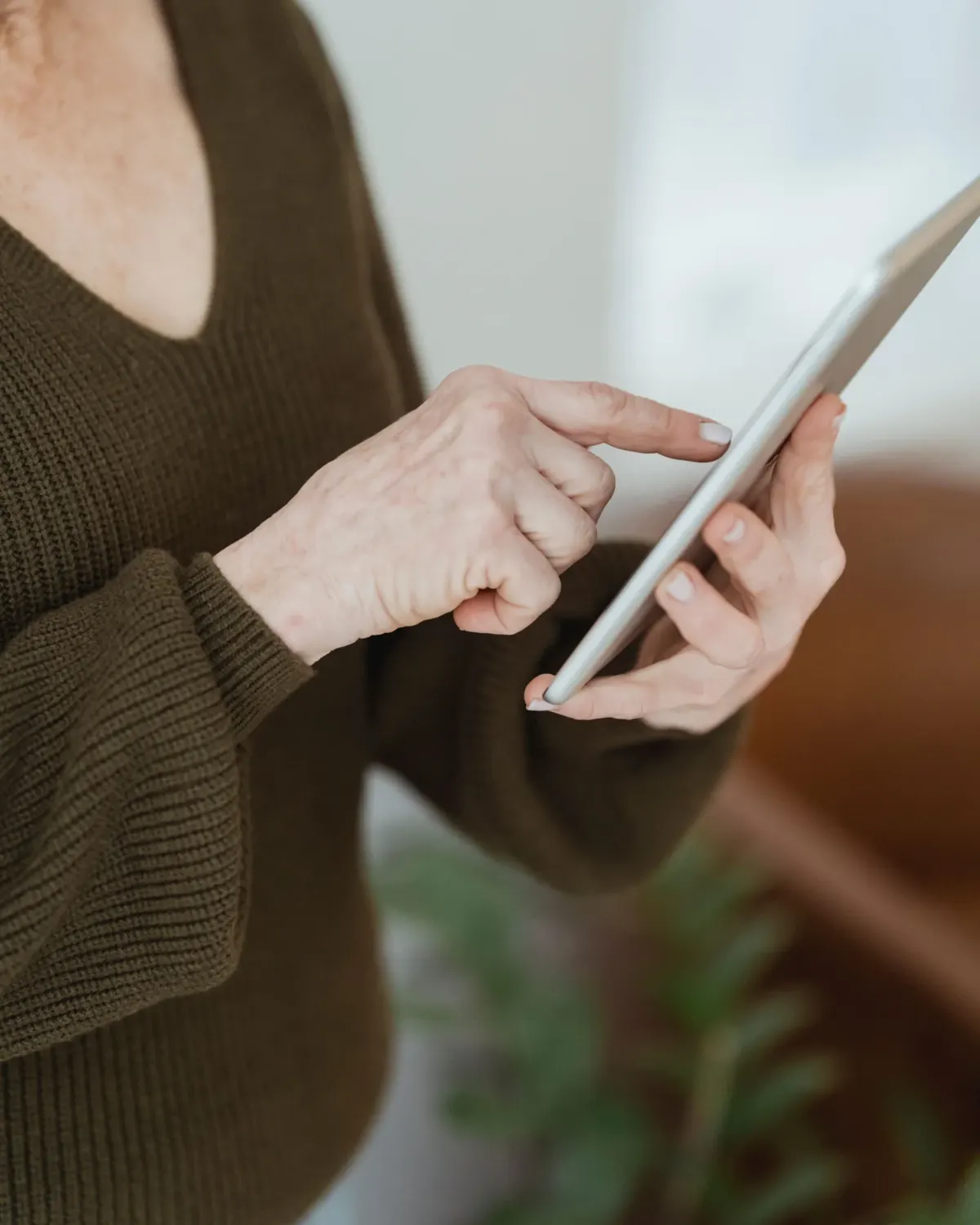 Close-up of an older woman's hands as she taps the screen of a tablet