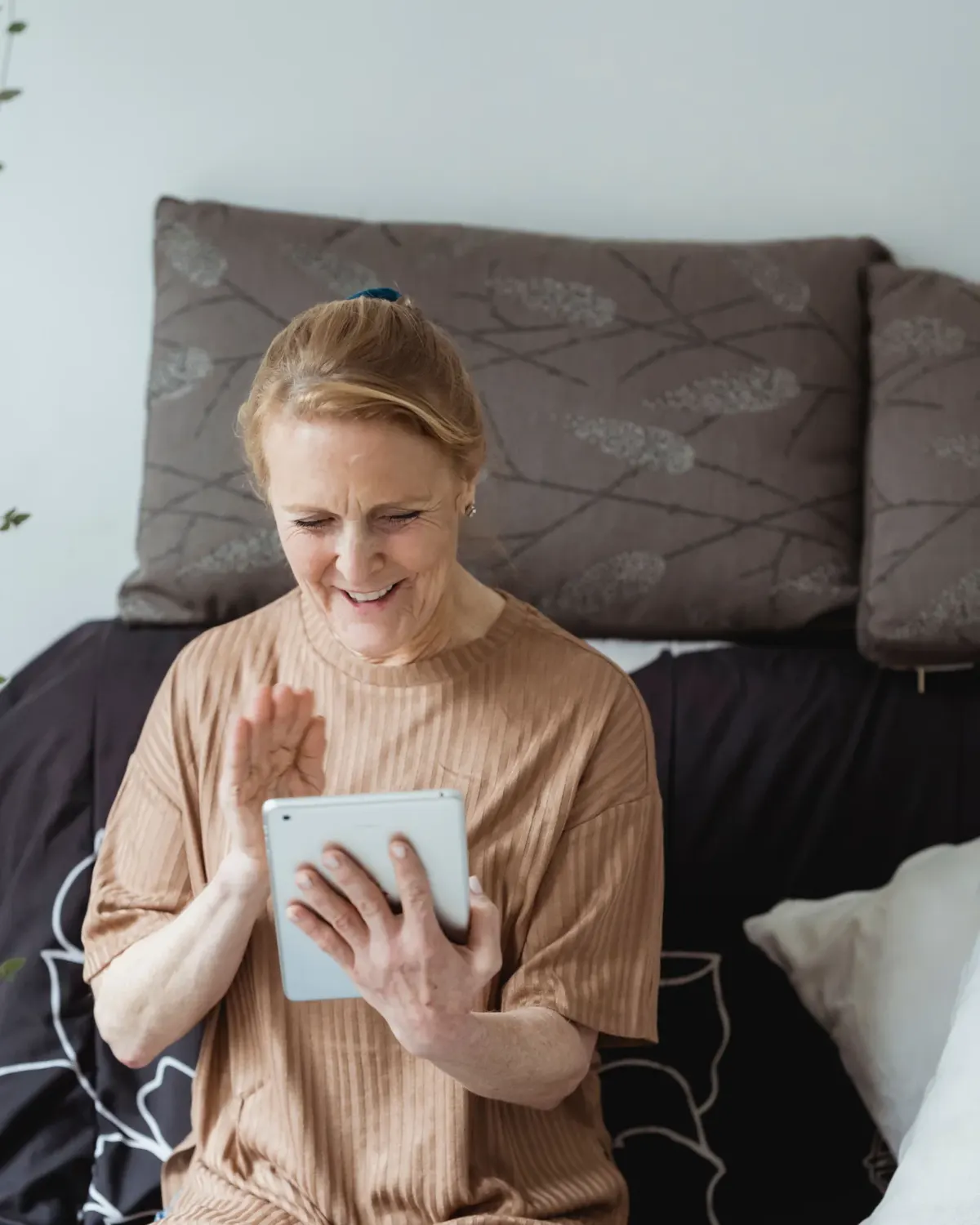 An older woman laughing and waving at the screen of her tablet