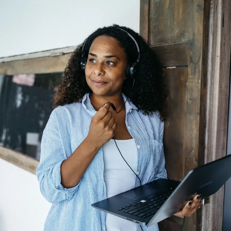 A smiling woman wearing a headset and holding a laptop