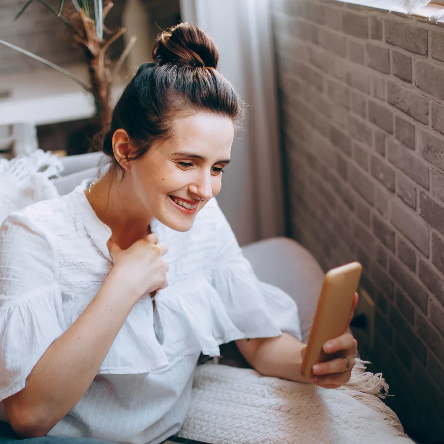 A young woman on a sofa, smiling as she looks at her phone